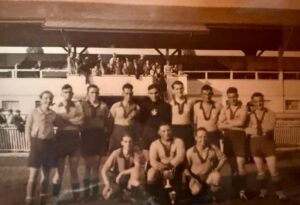 Ancienne équipe du FC Gland posant avec un trophée devant la tribune du stade, photo historique du club.